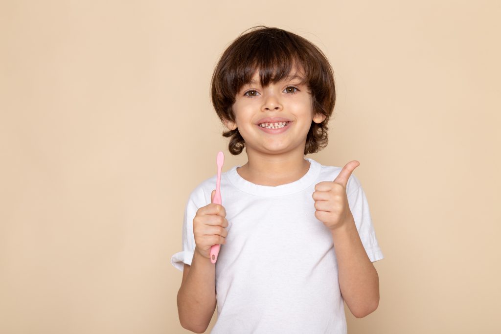 Teaching Kids to Brush Can Be Fun and Effective 2 front portrait view smiling boy cute adorable sweet white t shirt pink wall